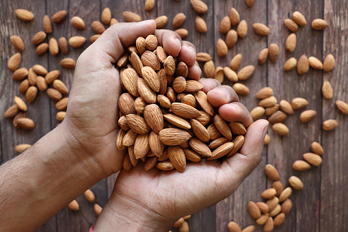 Stock photo showing close-up view of a heap of almonds that are piled high on a woodgrain background. Raw almonds are considered to be a very healthy snack food, containing vitamin E, antioxidants and protein, and boasting a list of health benefits while aiding blood sugar control.