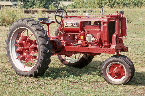 An old red tractor sits alone in a prairie field of tall grass.