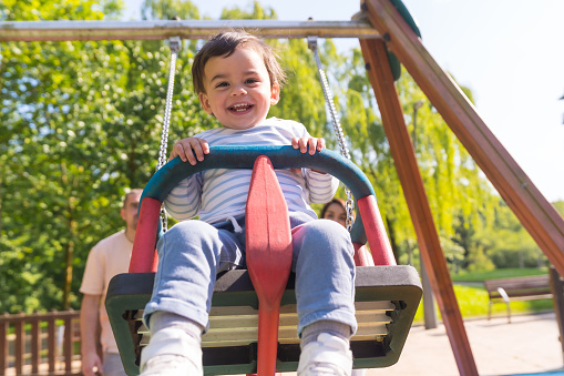 Frontal view of a happy baby boy in a swing laughing next to his parents