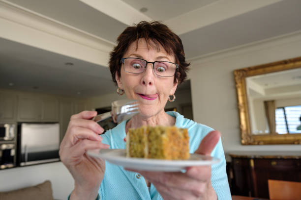 Senior woman indoors looking excitedly down at a slice of cake on her plate.