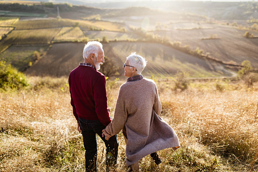 Rear view of carefree mature couple talking while walking down the hill in autumn day.
