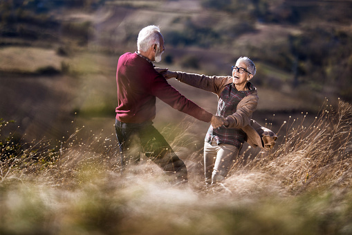 Playful senior couple holding hands and having fun during autumn day on a hill. Focus is on woman. Copy space.