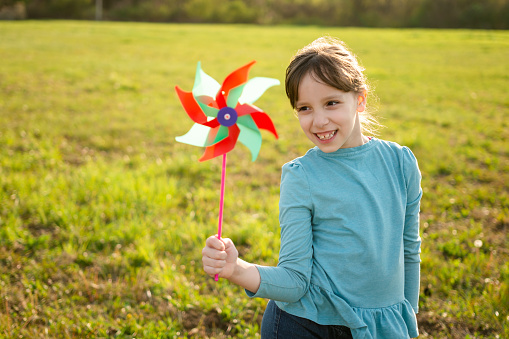 Cute happy little girl playing with a pinwheel outside.