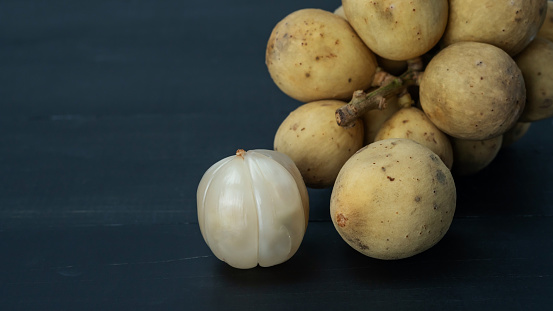 Lansium parasiticum fruit on a black wooden table.