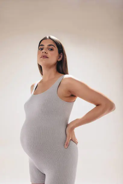 Expecting mother in her third trimester showcases her baby bump while practicing prenatal care in a studio. She wears fitness clothing, exercising for the health and wellness of her unborn baby.