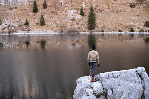 Adventure Survival Expert Woman Observing Wilderness from a High Position near a Lake in Winter