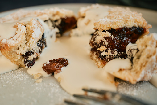 Close up of a split open Mince Pie covered in pouring cream.