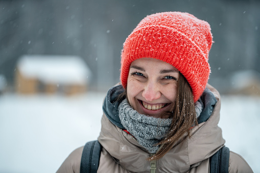 Joyful woman wearing warm clothing outdoors at snowing day, close-up portrait