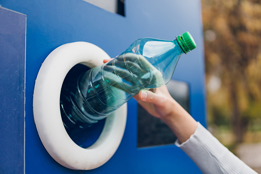 Young woman recycling plastic bottles in a machine
