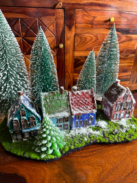 istock Image of scenic Christmas village display, artificial plastic Christmas trees on artificial grass and snow surrounded by illuminated miniature houses, winter scene on wooden cabinet, focus on foreground 1834703916