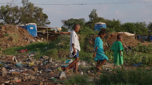 Slow motion. Poverty , three poor Black African children playing around portable toilets and stinking effluent water in an informal settlement