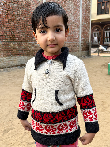 Stock photo showing close-up view of young child standing outside a residential building, looking at camera posing for a photograph.