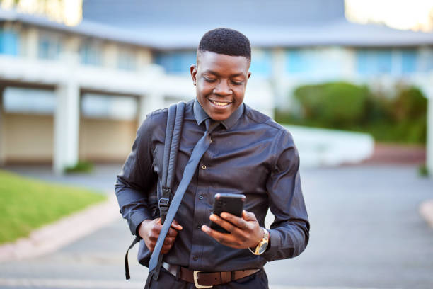 joven hombre de negocios negro caminando afuera con teléfono celular y bolsa de computadora portátil - quit scene fotografías e imágenes de stock