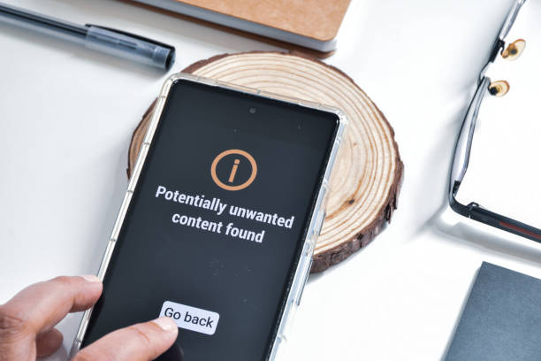 istock Woman hand on her smartphone showing message potentially unwanted content found. Virus and threat protection concept. 1834733416