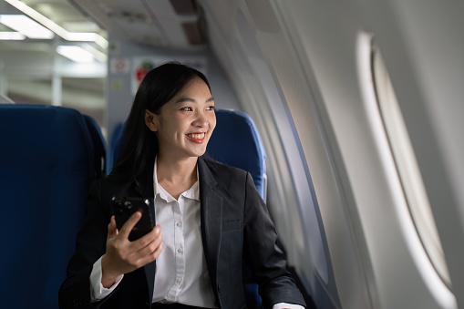 businesswoman flying and working in an airplane in first class, sitting inside an airplane using mobile.