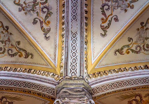 Detail of the vaulted ceiling of the chapel decorated with paintings and religious frescoes of angels and allegorical figures with human skulls creating ornaments.