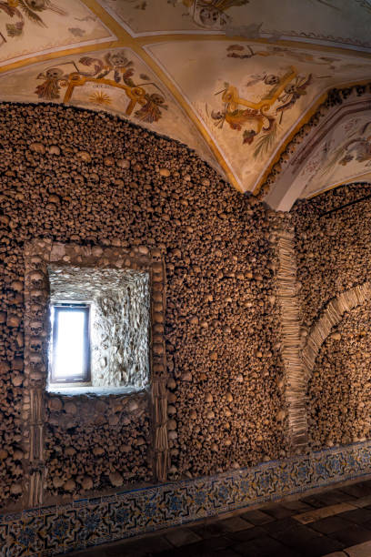 istock Vaulted ceiling with allegorical religious paintings and the wall decorated with human bones and skulls with daylight entering through a window decorated with skulls. Evora, Portugal. 1834761966