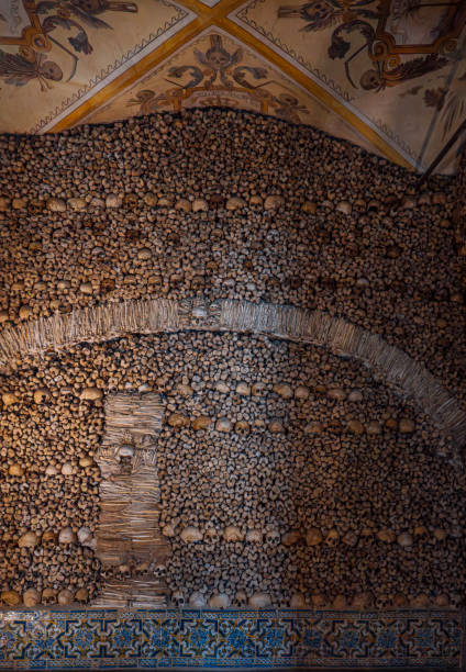 istock Wall of human bones and skulls creating an arch-shaped design and vaulted ceiling with religious allegorical paintings from The Chapel of Bones. Evora, Portugal. 1834763565