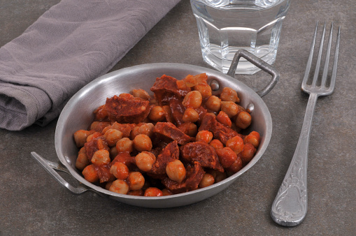 Chickpeas with chorizo in tin dish with fork and glass of water