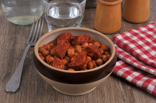Chickpeas with chorizo served in a bowl with a fork and a glass of water