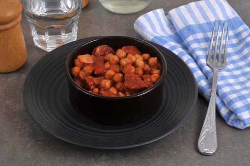Chickpeas with chorizo served in a ramekin with a fork and a glass of water