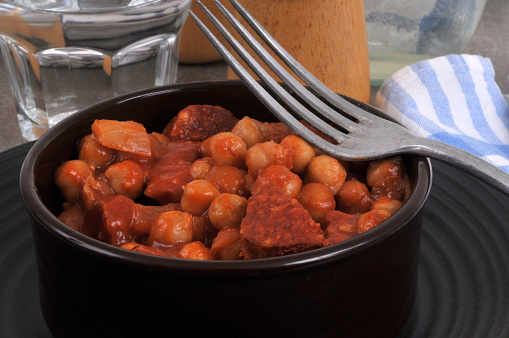 Chickpeas with chorizo served in a ramekin with a fork and a glass of water closeup