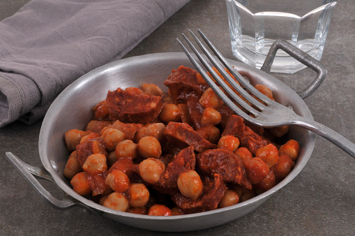 Chickpeas with chorizo in tin dish with fork and glass of water