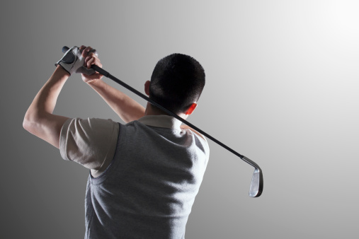 Young golf player swinging, rear view