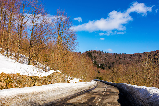 old road pass through snow covered forested hills. mountainous winter landscape on a sunny day beneath a blue sky with clouds