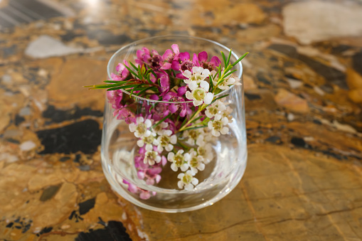 A small glass on a table with tiny flowers inside.