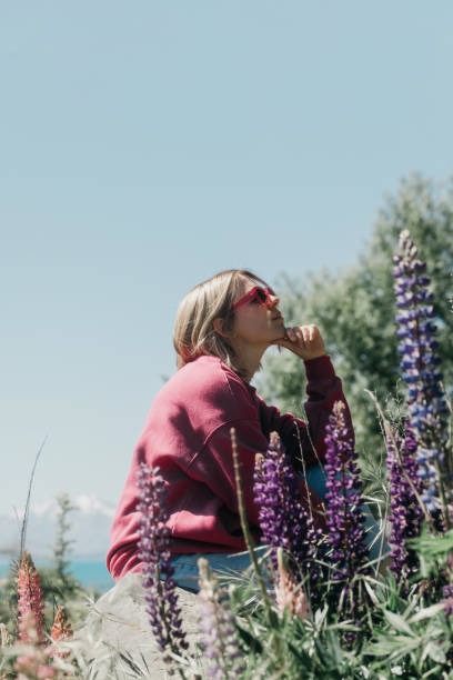 eine frau sitzt in der natur neben blühenden lupinen mit blick auf die berglandschaft. reise - lupine single flower flower blue stock-fotos und bilder