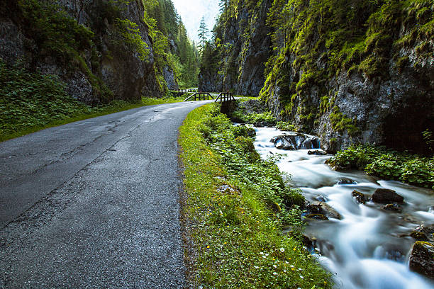 Long Exposure of the road alongside the creek at Serrai di Sottoguda. A gorge on the Dolomites near Marmolada in Italy. A small bridge in the distance