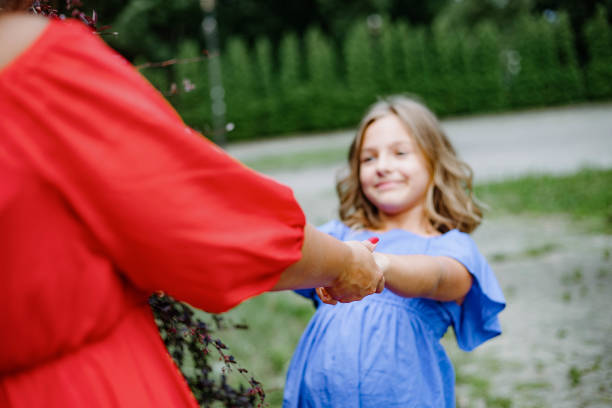 śliczna dziewczynka w wieku 10-11 lat w niebieskiej sukience uśmiecha się, kręci trzymając się za ręce nierozpoznawalnej mamy. - 10 11 years child little girls offspring zdjęcia i obrazy z banku zdjęć