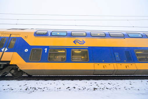 Intercity train of the Dutch Railways driving through the snow on a cold day in the Veluwe nature reserve in winter.