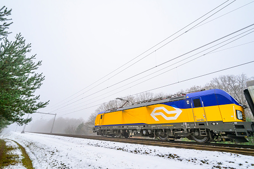 International train of the Dutch Railways driving through the snow on a cold day in the Veluwe nature reserve in winter.