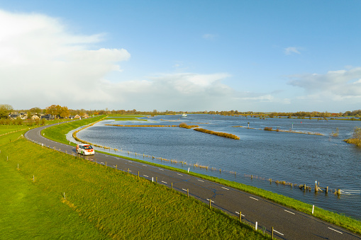 Volkswagen ID.Buzz for PostNL postal services full electric delivery van driving on a levee along the flooded river IJssel near Zalk village in Overijssel. The floodplains are overflown after a long period of heavy rain upstream during autumn.