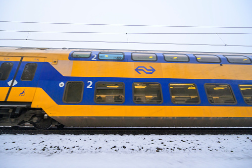 Intercity train of the Dutch Railways driving through the snow on a cold day in the Veluwe nature reserve in winter.