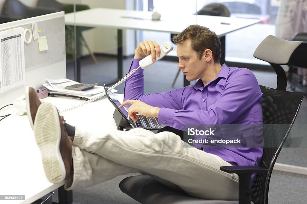 bad sitting posture at desk in office Young businessman caucasian in his office on phone working with tablet - bad sitting posture Activity Stock Photo