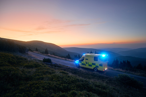 Ambulance car of emergency medical service mountain road against sunrise. Moody sky with copy space. Themes rescue, urgency and health care.