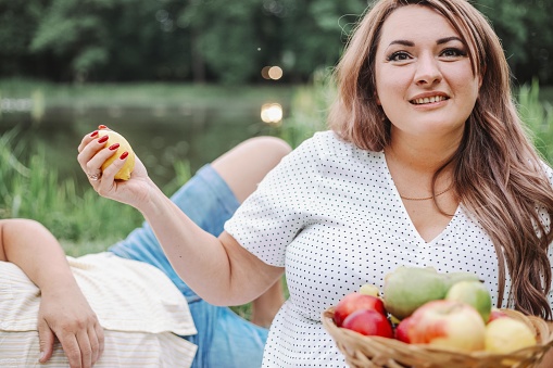 Charming woman in light dress holds plate of fruit at summer picnic. Proper nutrition. Vegan food.
