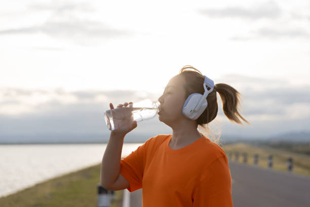 Asian woman drinking water while exercising outdoors.