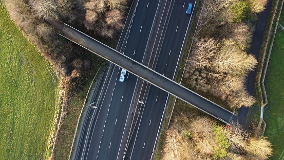 Top down aerial shot of a pedestrian overpass crossing a dual carriageway with cars passing underneath in Manchester, United Kingdom