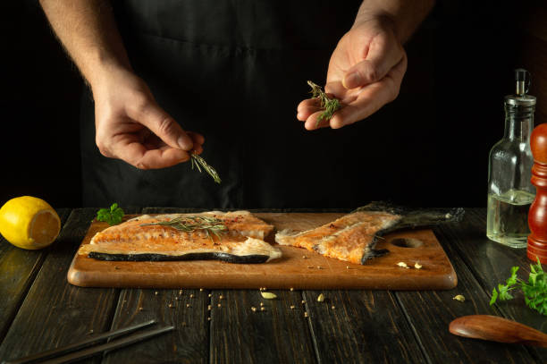 istock Chef preparing fresh red fish on the kitchen table in a restaurant. Before frying, fish steaks are seasoned with aromatic rosemary. European cuisine 1834901186