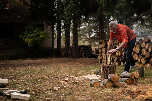 Lumberjack cutting firewood with axe outdoors in nature alone.
