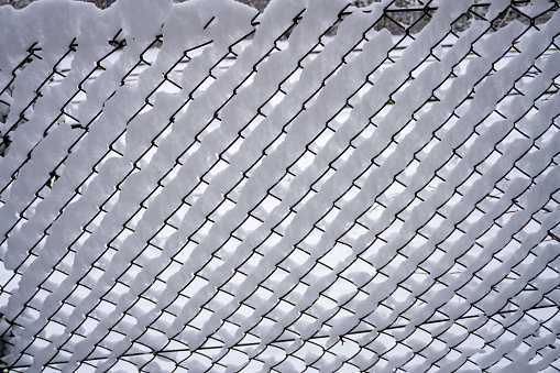 Winter Wonderland in the Midwest. Texture of snow on the fencing net. Metal wire mesh covered with snow in winter. High quality photo