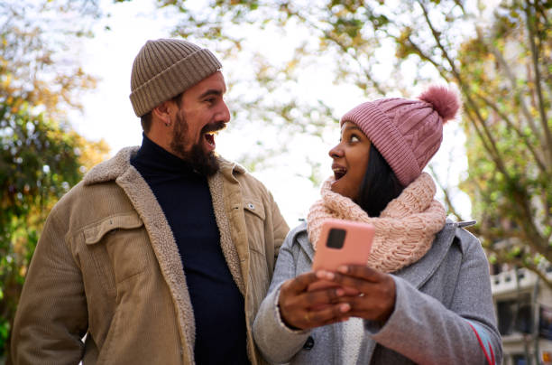 istock Young multiethnic couple using phone, looking at each other surprised. People winning online gifts. 1834905784