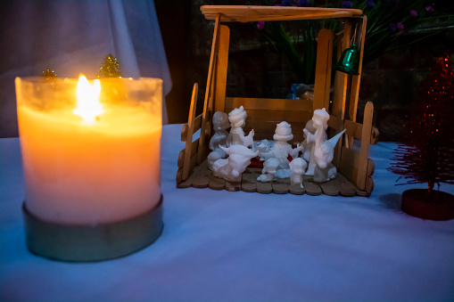 In the warm, dim glow of flickering candles, a nativity scene is tenderly arranged on a rustic wooden table, casting a serene ambiance far beyond its immediate surroundings. The figures, meticulously carved and rich with detail, encapsulate the humble yet profound moment of a timeless birth. Mary and Joseph, portrayed with reverent expressions, gaze upon the Christ child with a blend of awe and love, while the Three Wise Men stand at a respectful distance, their gifts held in outstretched hands as an offering. Shadows dance across the wall, echoing the tranquil yet joyous spirit of this holy tableau. This image, a harmonious blend of shadow and light, tradition and tranquility, invites viewers to reflect on the deeper meaning of the holiday season, emphasizing a silent night where hope was rekindled in a manger under starlit skies