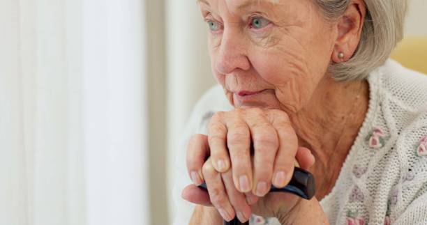 先輩の女性は、自宅のソファで思い出を思い出し、退職後にリラックスするために杖をつきます。アルツハイマー病や関節炎の介護施設にいる障害のある重篤または悲しい高齢者または老婦� - old senior adult women tired ストックフォトと画像
