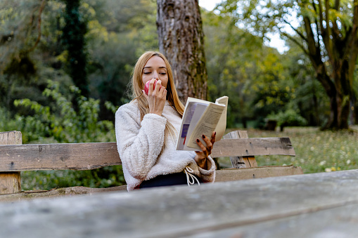 Nourishing both body and mind, a young woman nibbles on an apple, finding literary fulfillment on a bench surrounded by the soothing embrace of nature