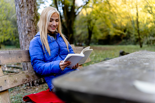Immersed in the wonders of nature, a young woman finds solace on a bench, delving into the pages of a captivating book